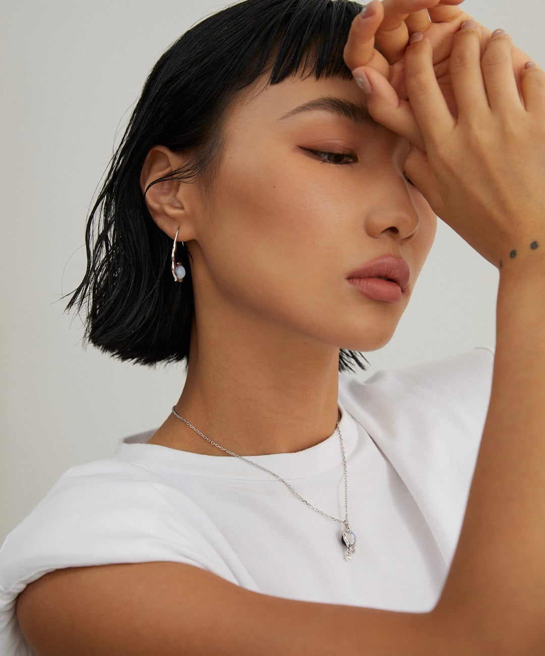 A model is wearing the dual-sided Lune Flux Earrings, showing the opal side.