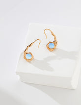 A pair of sculptural 18K gold vermeil earrings featuring a reversible design with opal on one side, displayed on a white textured block.