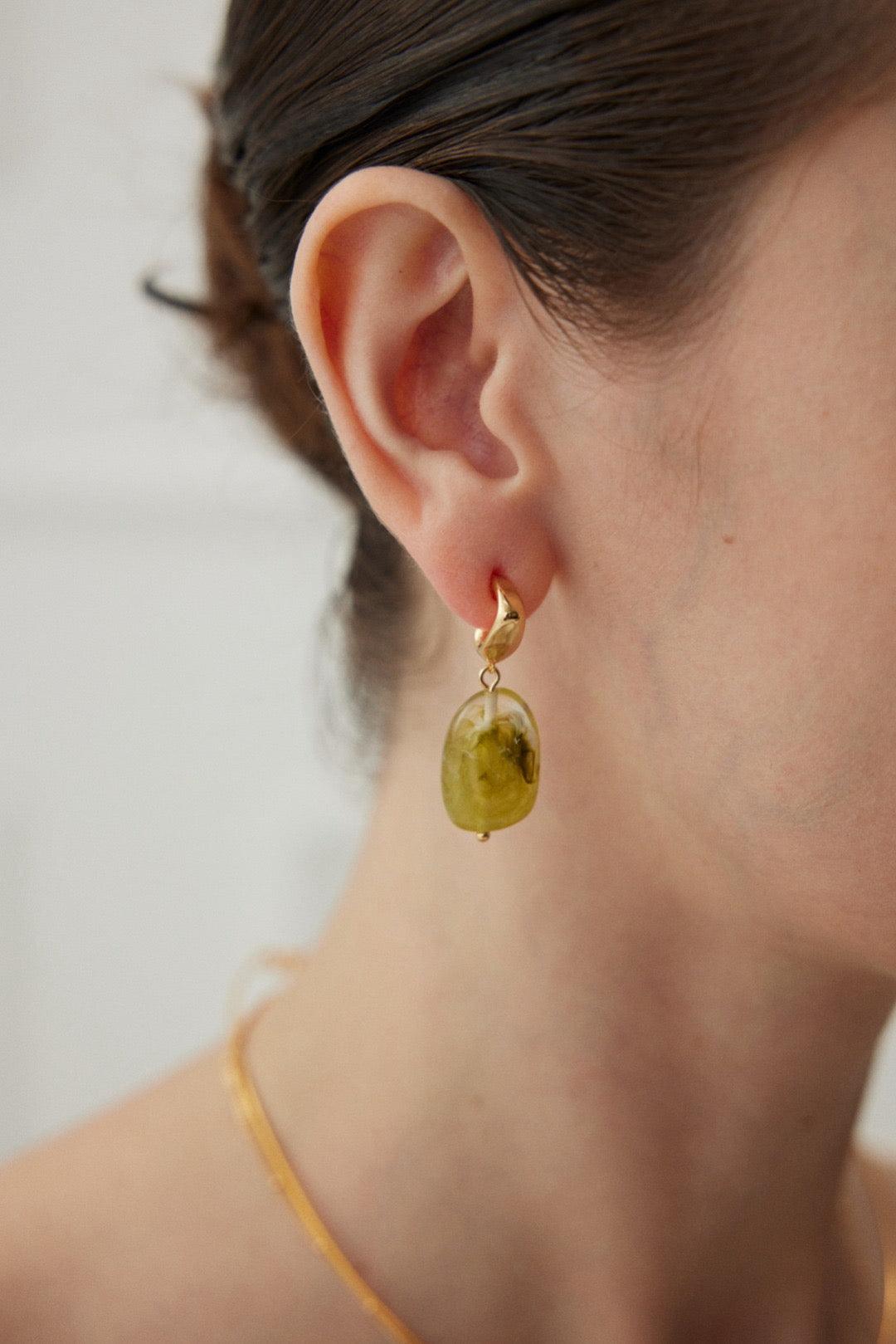 A person wearing gold drop earrings with green resin.