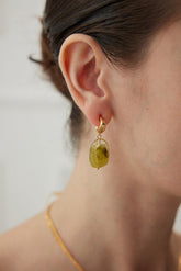A person wearing gold drop earrings with green resin.