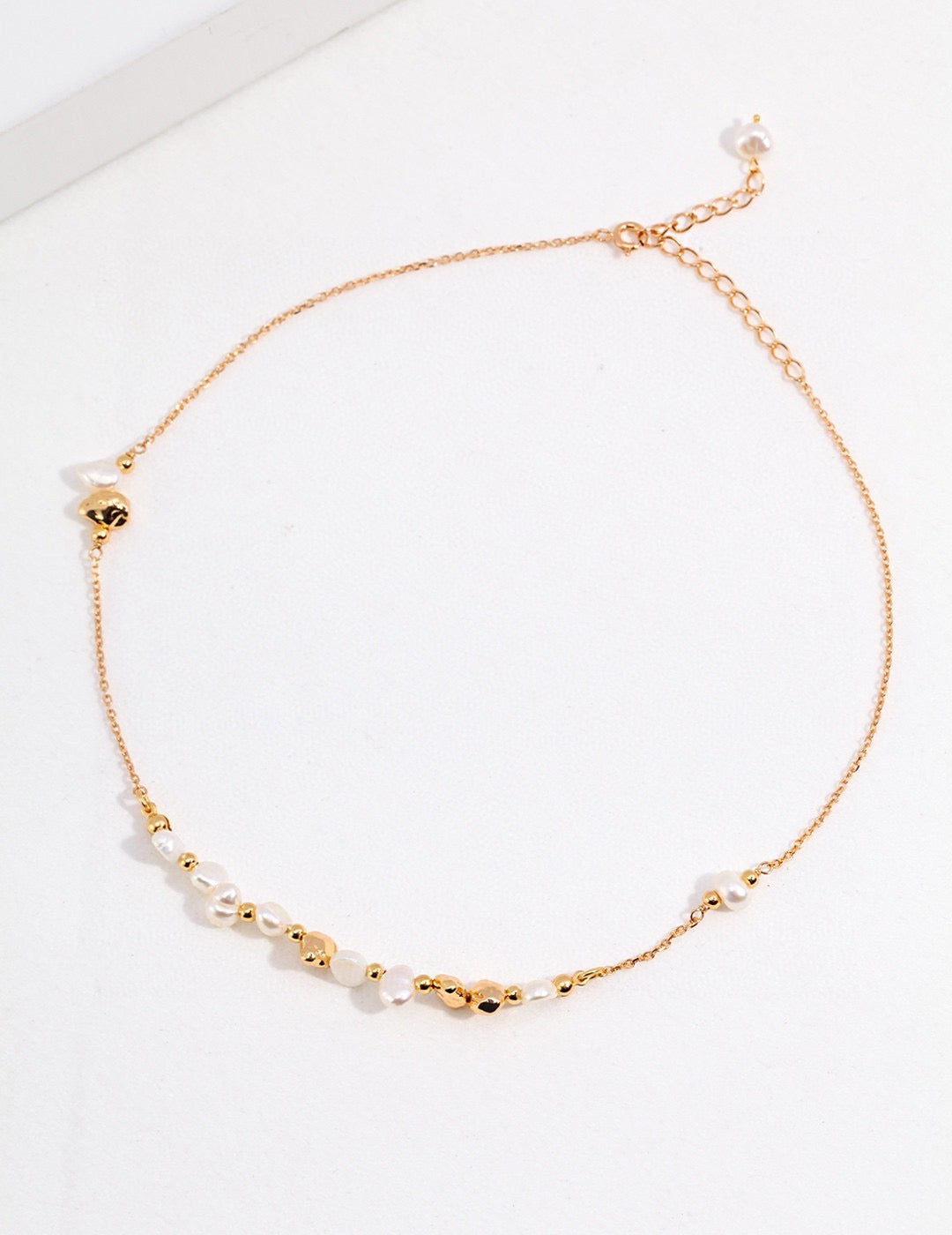 Minimalist gold necklace with small beads on a white background