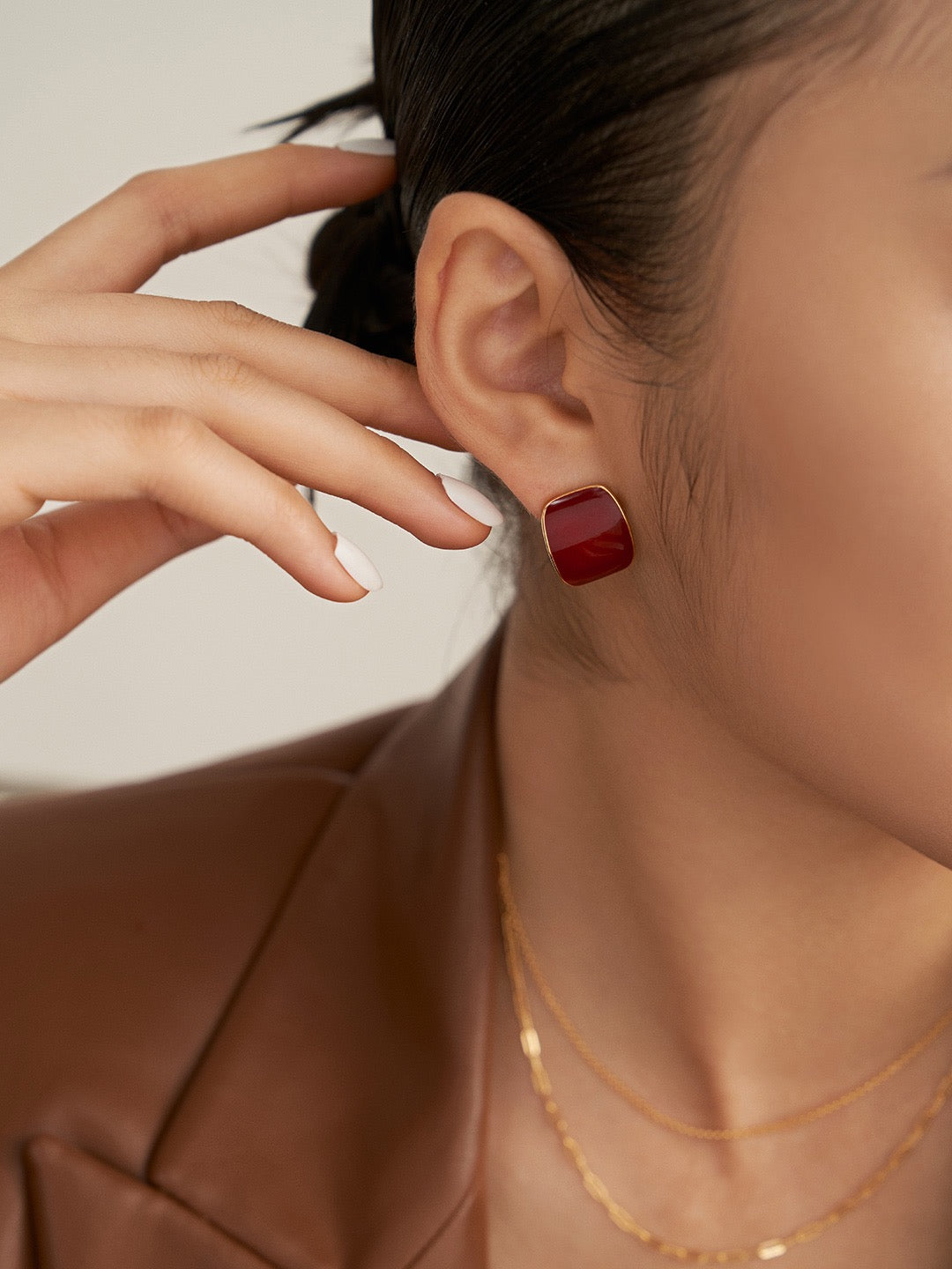 Close-up of a person wearing a red square earring with a neutral background