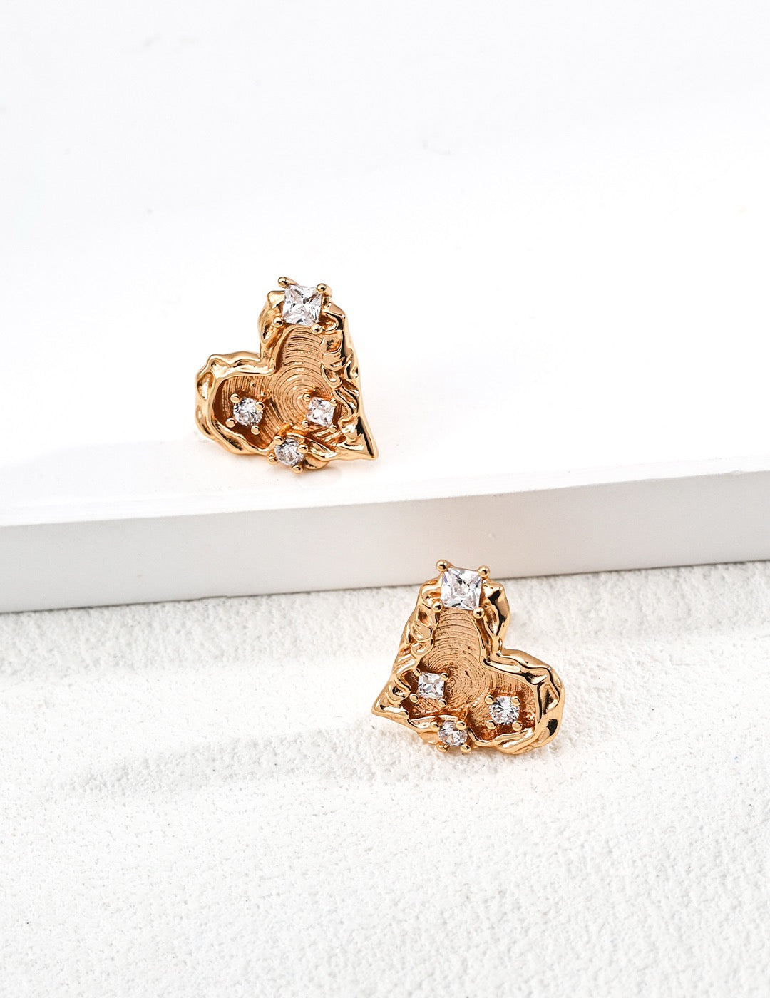 Molten gold heart-shaped stud earrings with textured finish and cubic zirconia accents, displayed on a white background.
