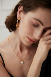 A person wearing a pearl pendant necklace with a crescent moon design, crafted from freshwater pearls and 18k gold vermeil.