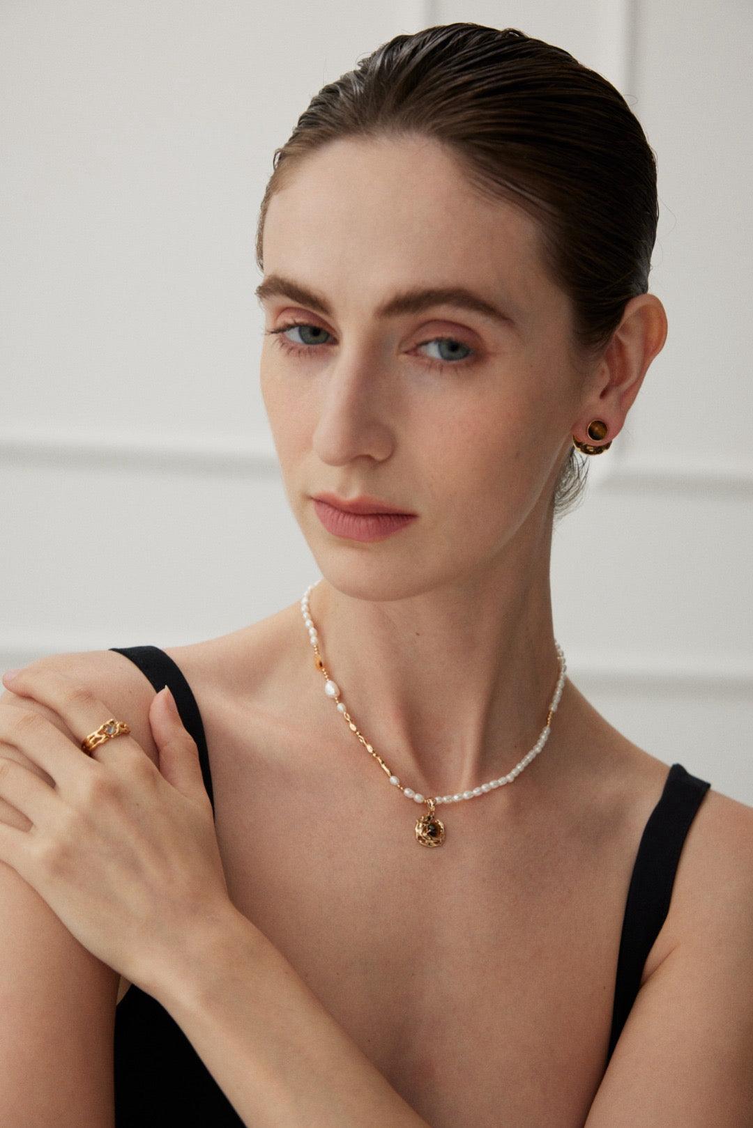 A woman wearing a black tank top showcasing a white beaded necklace with gold accents and a central agate stone.