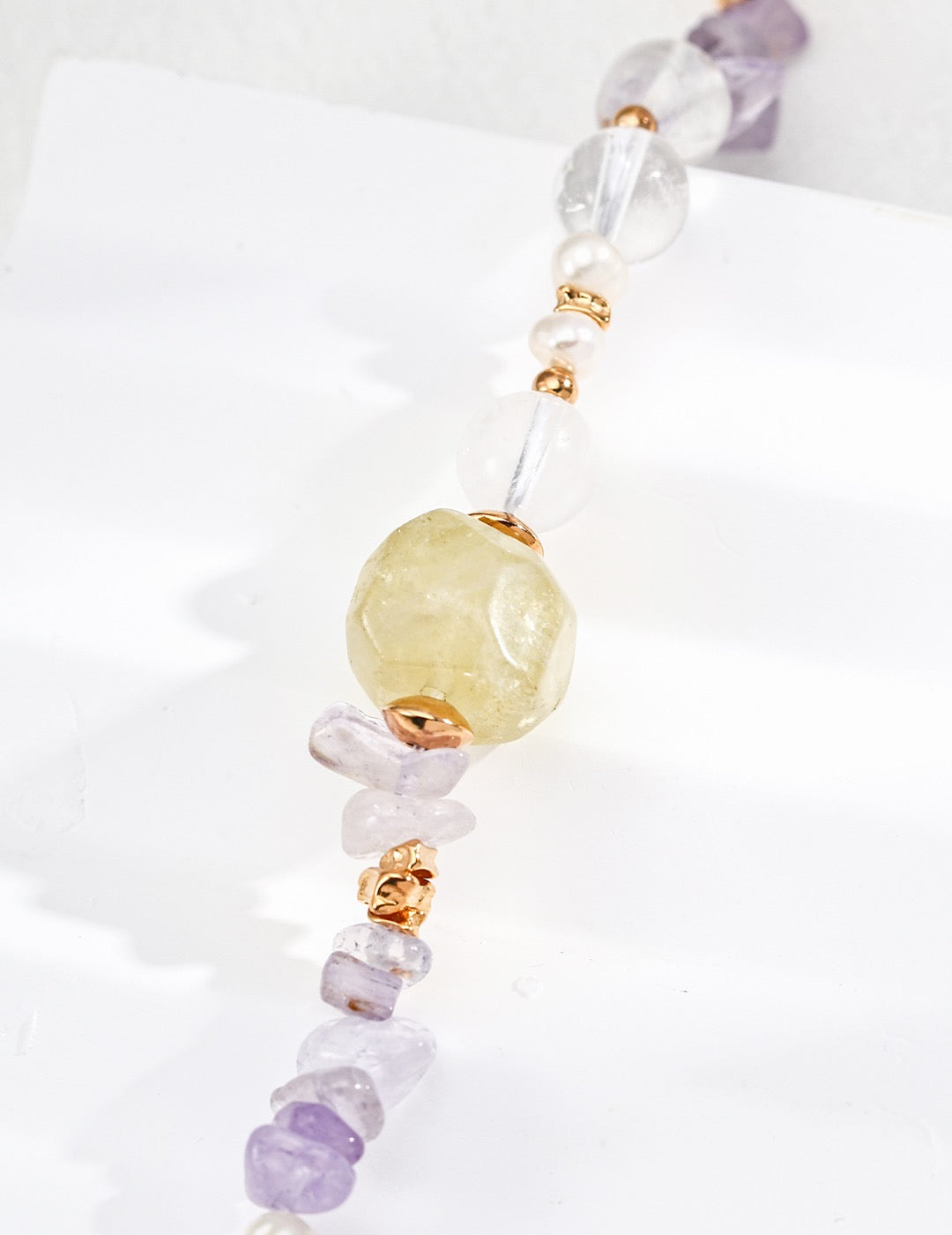 Close-up of an amethyst, rose quartz, and freshwater pearls bracelet with a citrine on a white background.