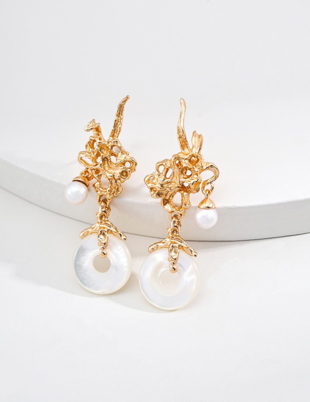 18K gold vermeil dangle earrings with coral-like metal design, freshwater pearls, and circular mother-of-pearl pendants, styled on a white round display.