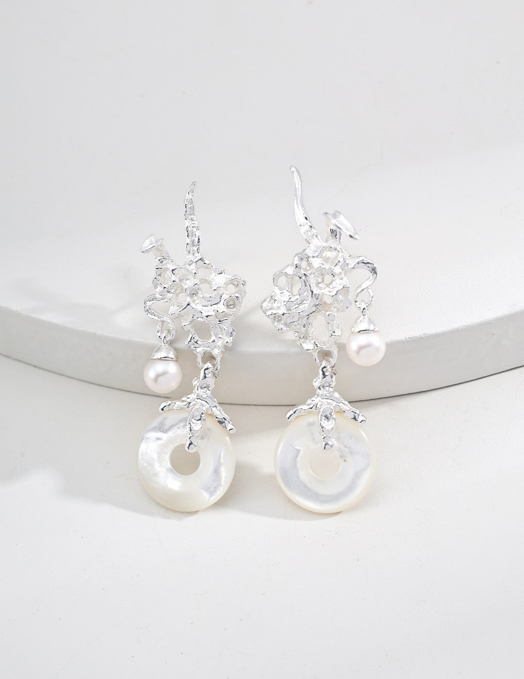 Sterling Silver dangle earrings with coral-like metal design, freshwater pearls, and circular mother-of-pearl pendants, styled on a white circle display.