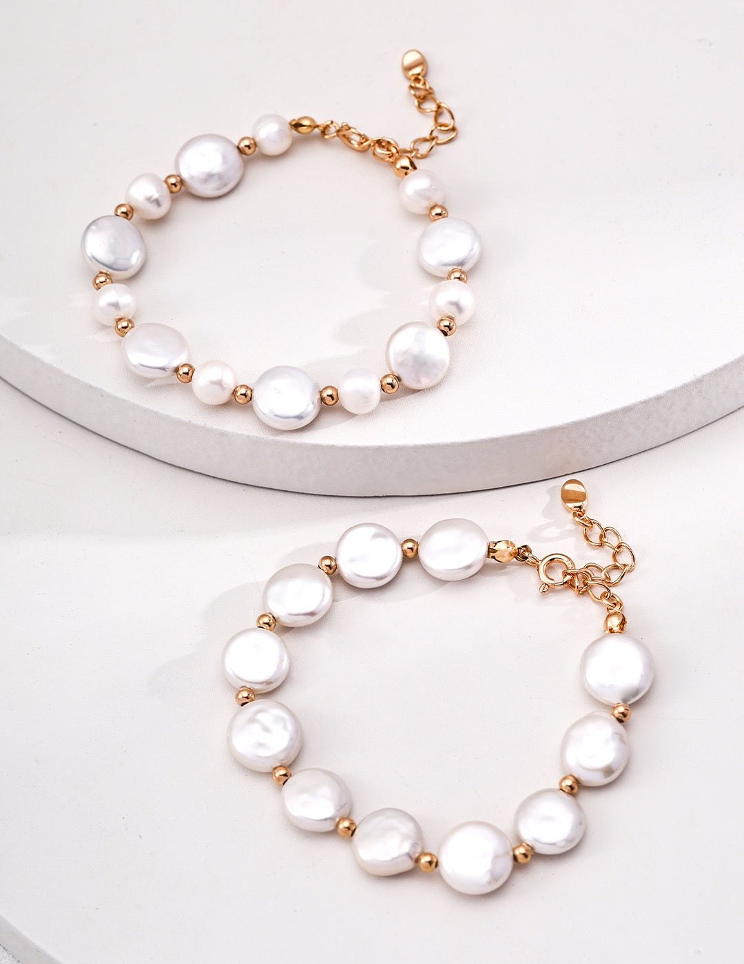 Two gold-accented freshwater pearl bracelets – one with large uniform pearls and one with alternating large and small pearls, shown on a minimalist white surface.
