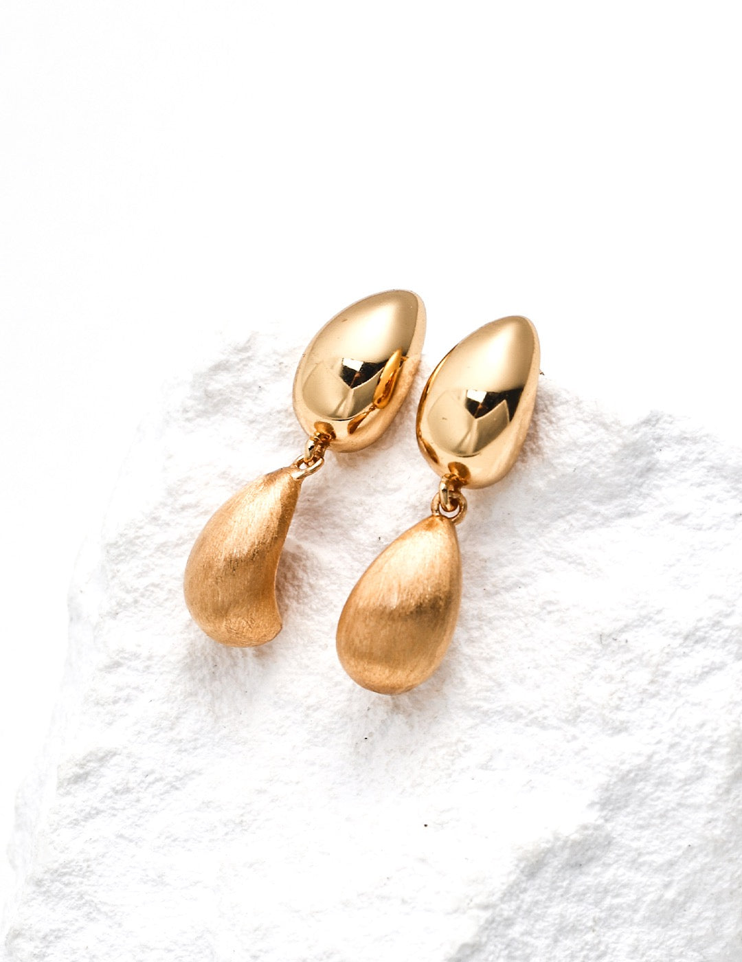 Gold teardrop earrings on a white textured surface