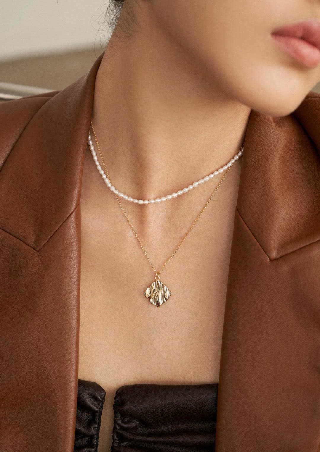 A close-up of the model is wearing the pearl-layered pendant necklace in a black dress and a brown leather jacket.