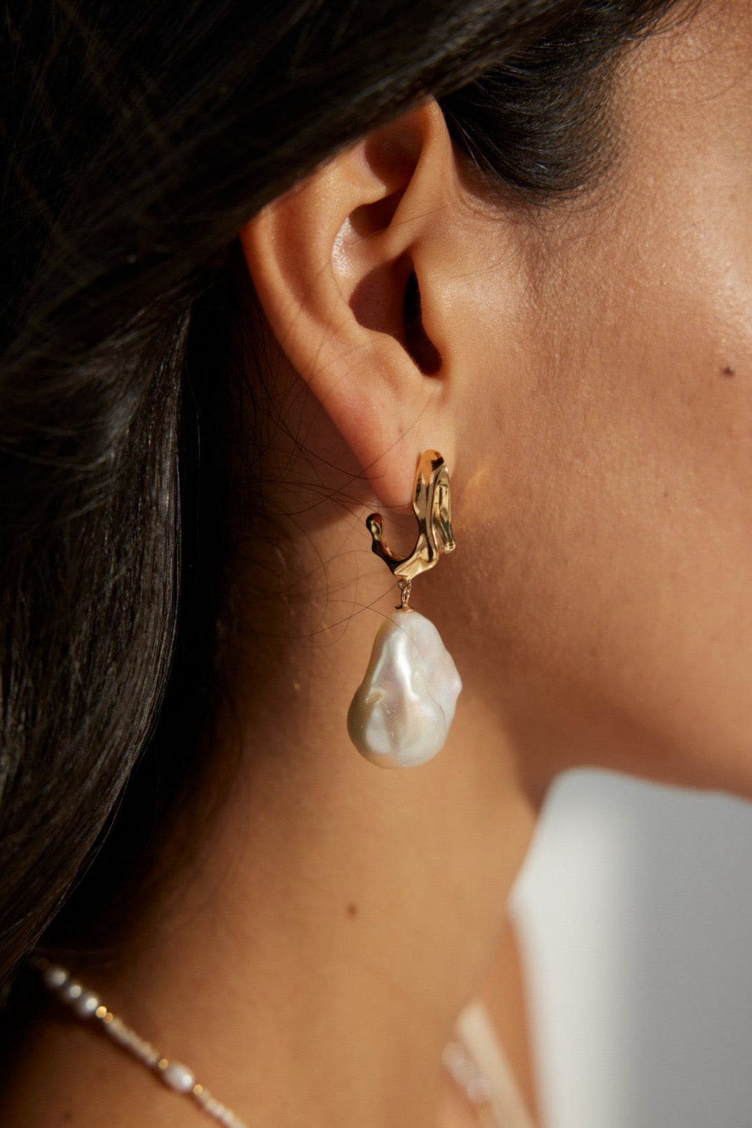 A close-up image of a woman's ear wearing a gold vermeil hoop earring with a large baroque pearl drop.