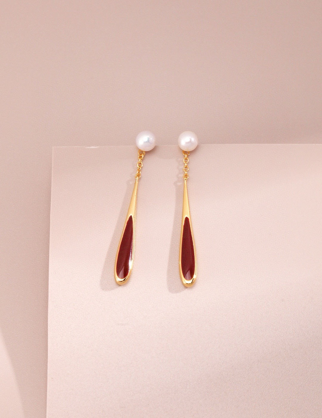 Pair of earrings with gold and red design on a light pink background