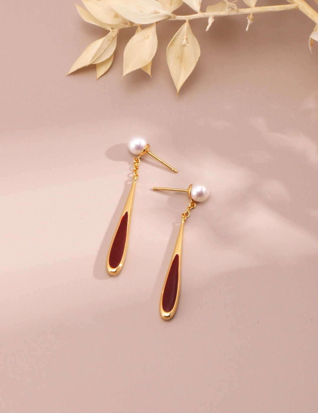 Gold earrings with red accents on a beige background
