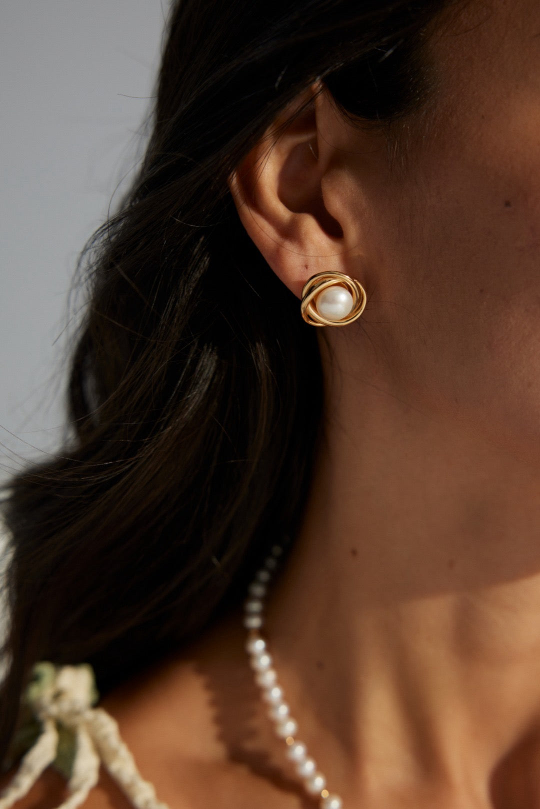 A close-up image of a woman's ear wearing a gold-colored pearl stud earring.