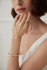 A person wearing a white top showcasing a gold-colored open ring with an enamel ornament on the finger.