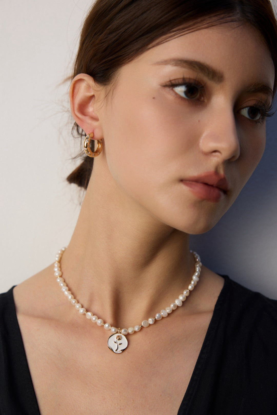 Woman wearing a pearl hand-painted rose pendant necklace and earrings against a neutral background