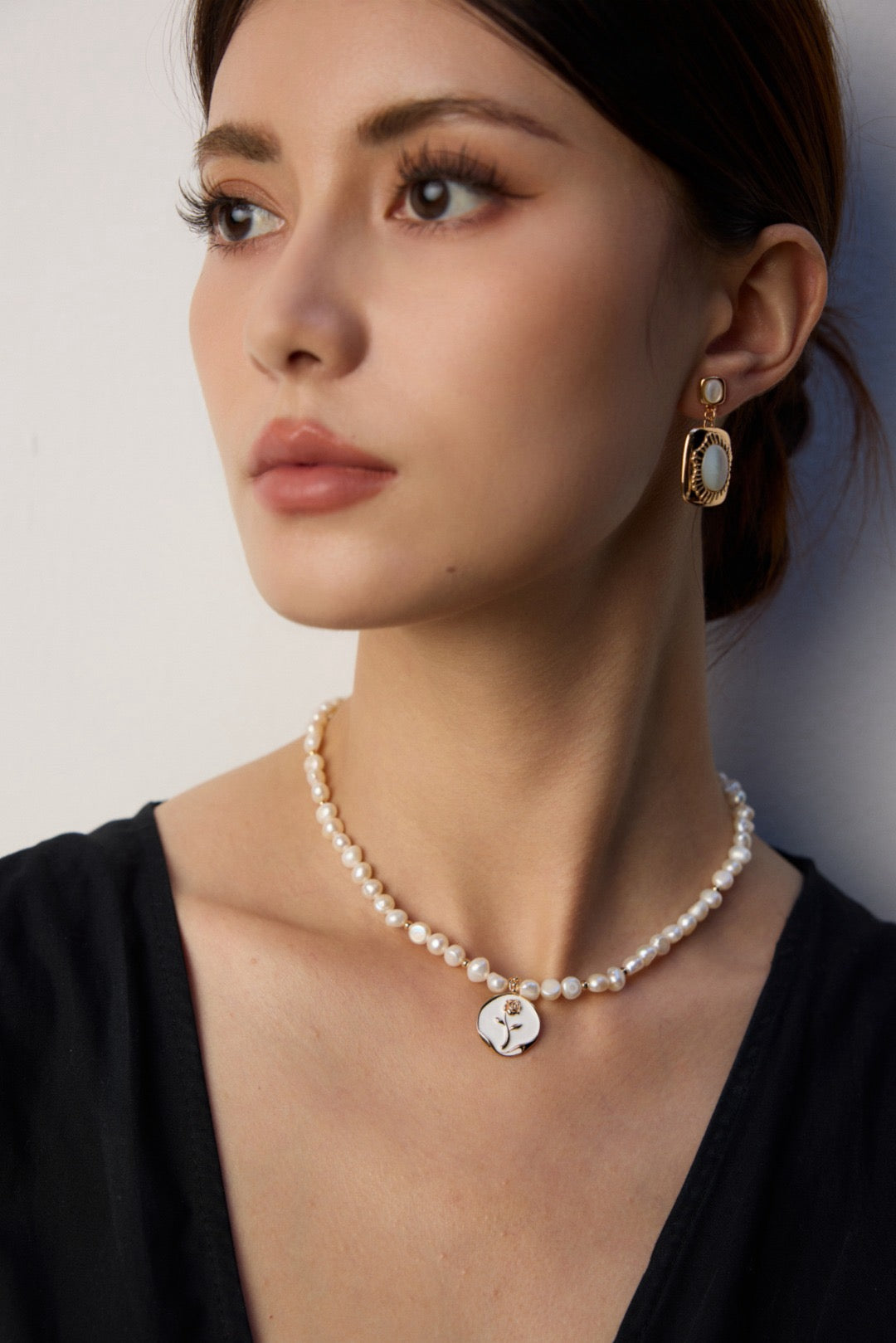Woman wearing a pearl necklace and earrings against a neutral background
