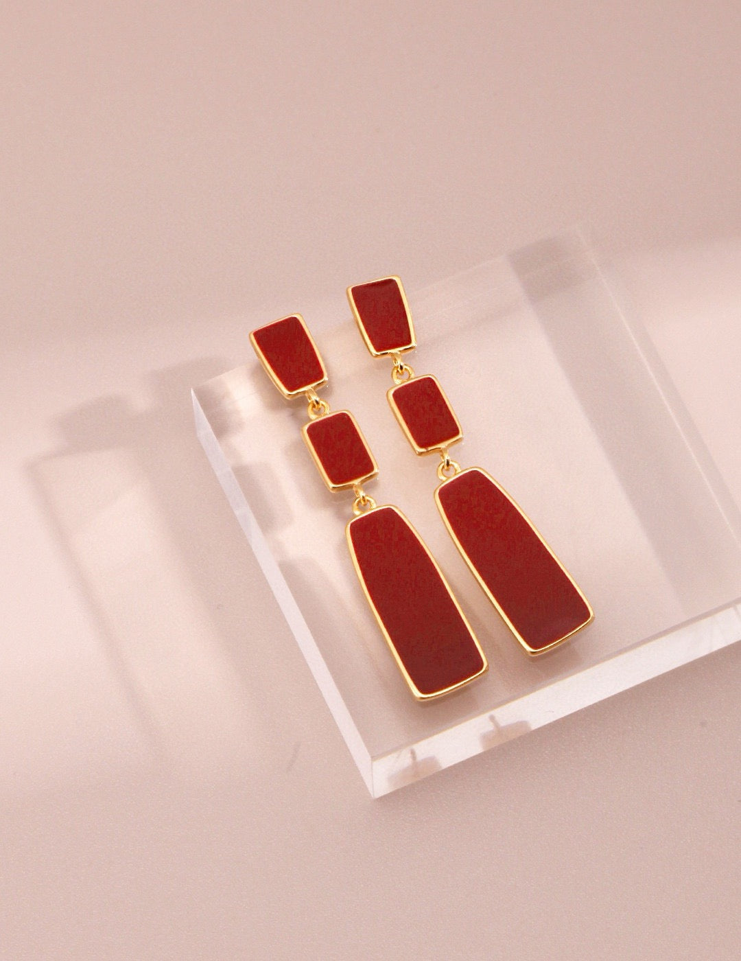 Red earrings with gold accents on a light pink background