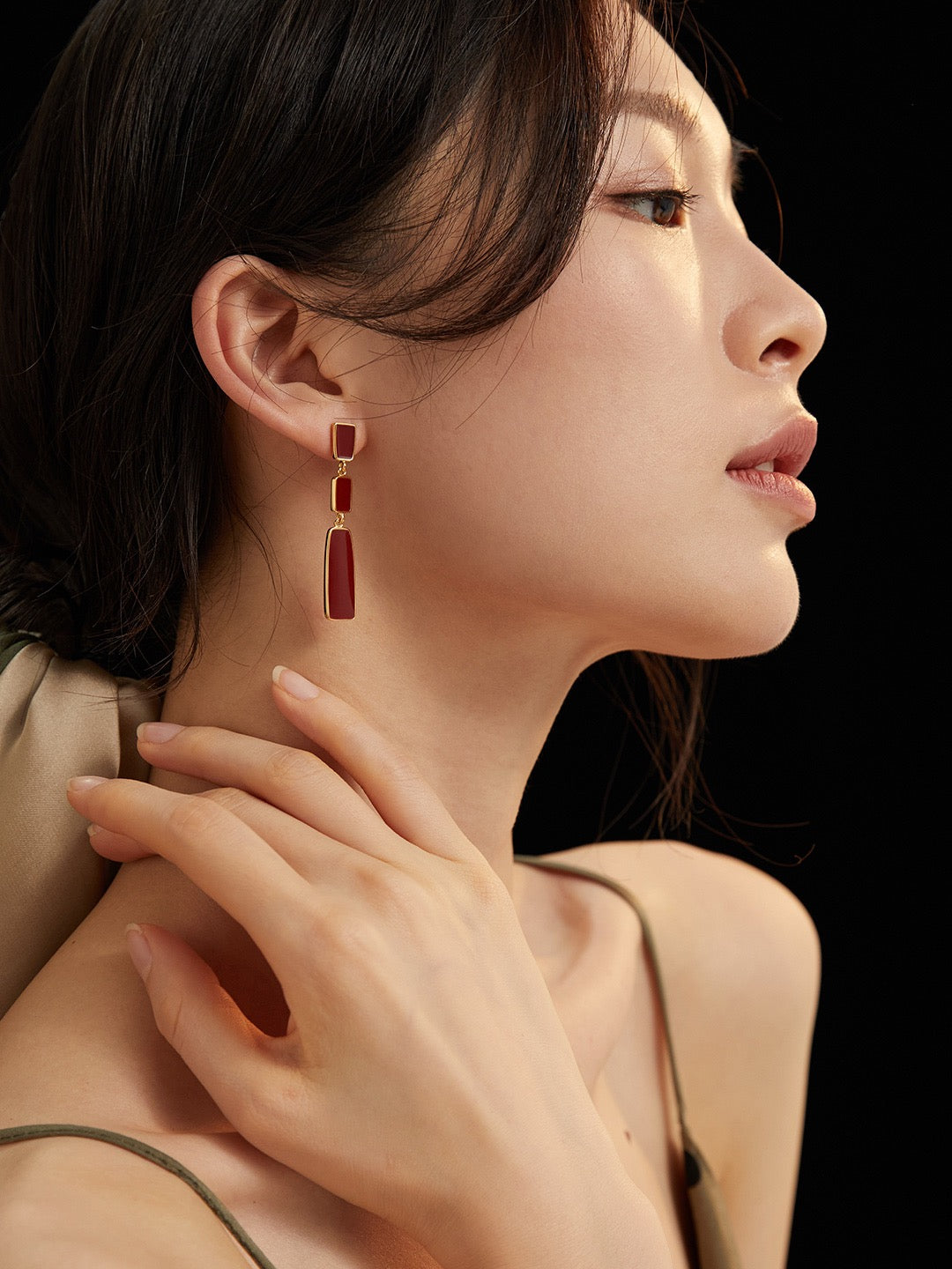 Close-up of a woman wearing a red enamel drop earring with a neutral background