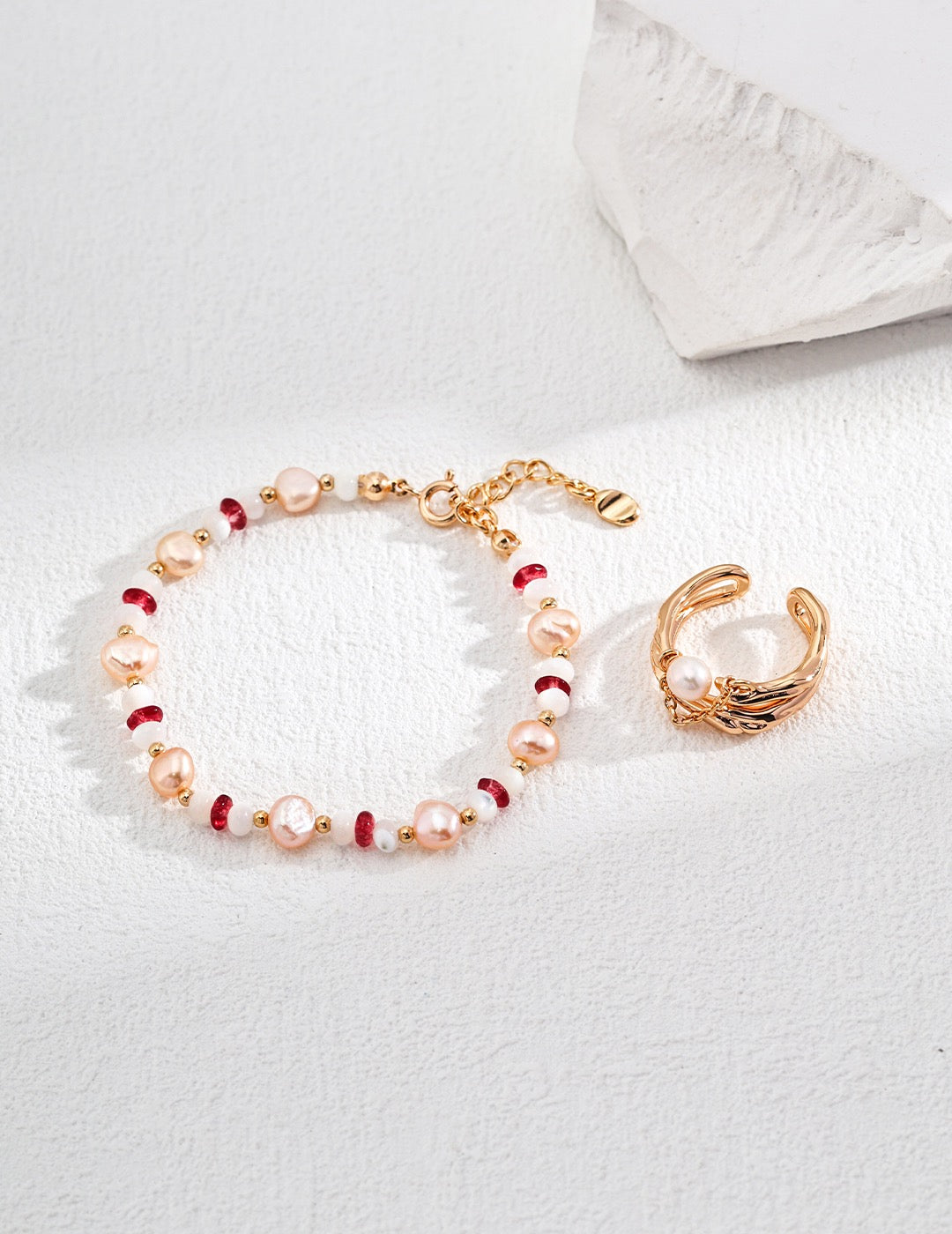 A gold vermeil bracelet featuring pink and red gemstones, and pink freshwater pearls displayed on a white surface.