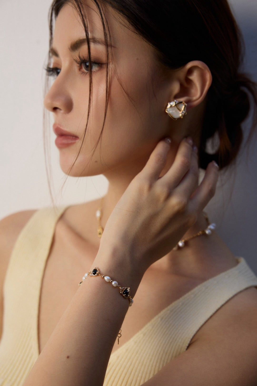 Woman wearing pearl earrings and bracelet against a light background