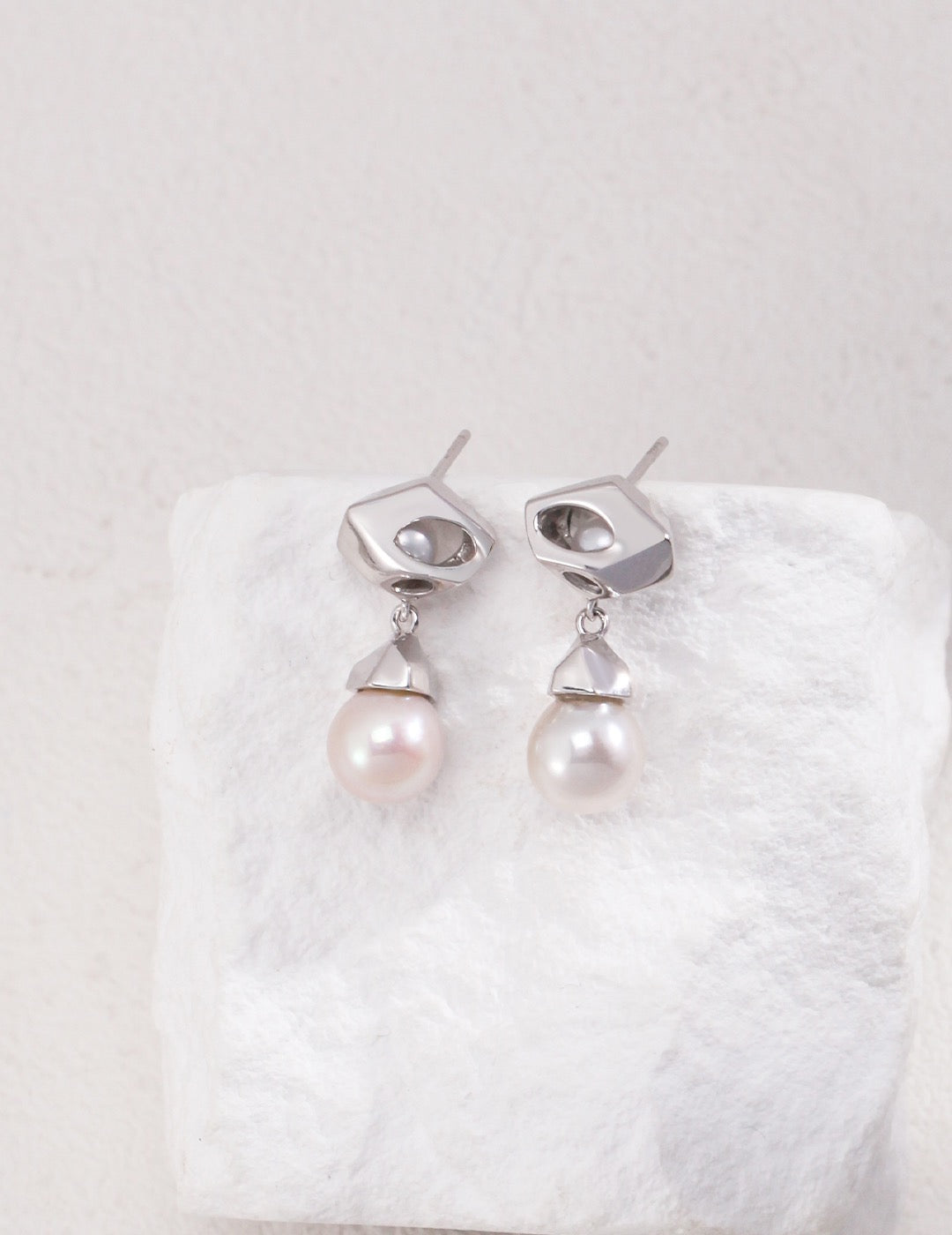 The Silver Luna Pearl Drop Earrings hanged on the white rock.