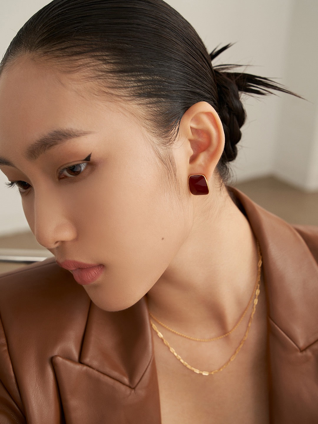 Woman wearing a gold necklace and red enamel stud earrings, looking to the side.