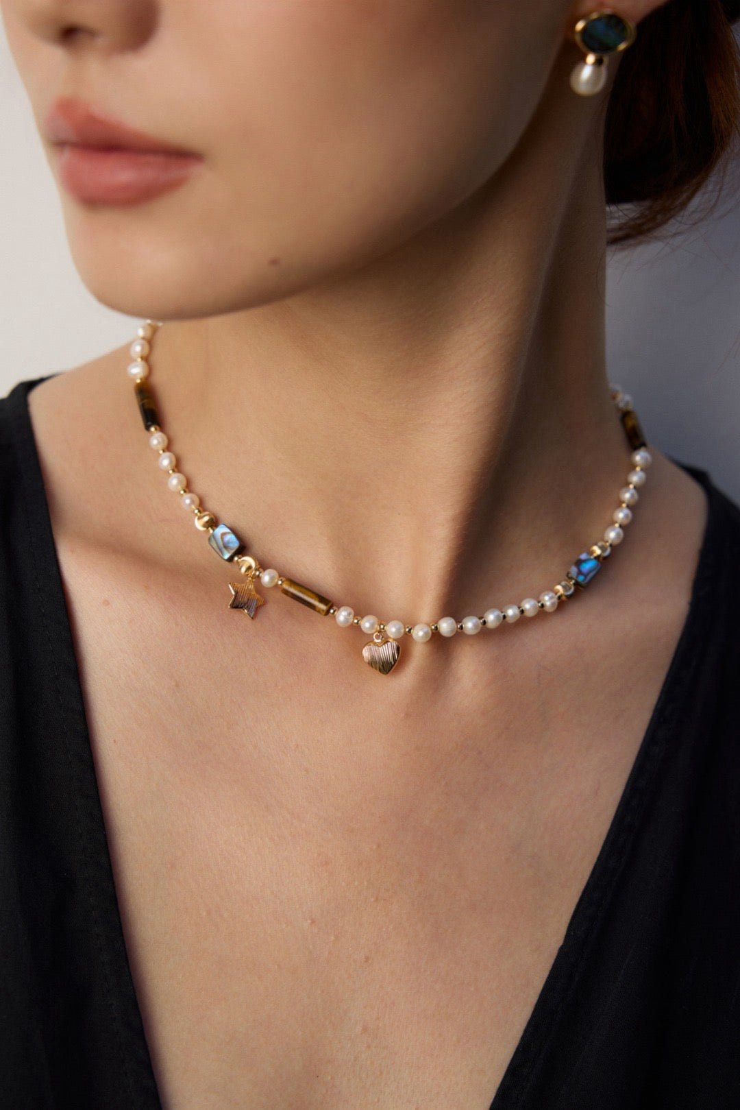 The model is wearing the Starlit Treasure Pearl Necklace with a black v-neck dress