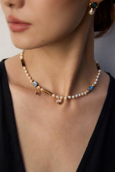 The model is wearing the Starlit Treasure Pearl Necklace with a black v-neck dress