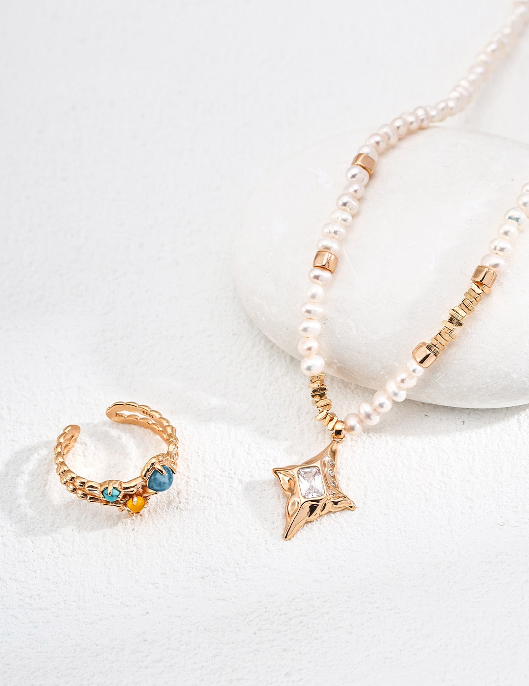 Gold ring with gemstones and a pearl necklace on a white surface
