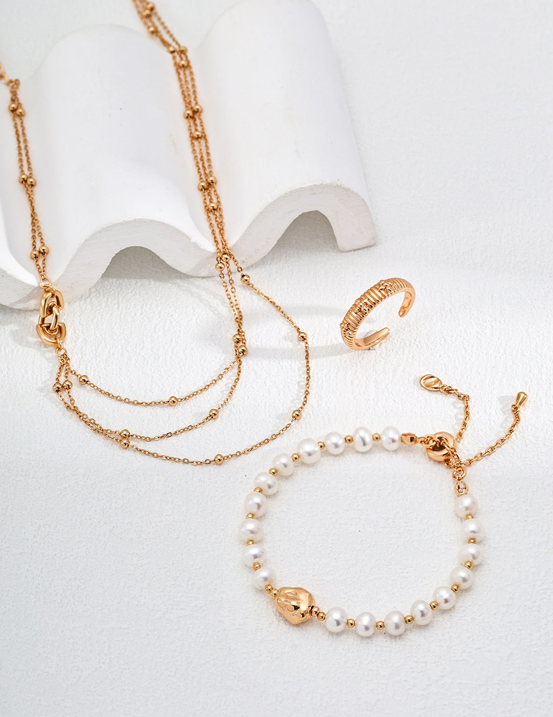 Gold necklace, bracelet, and ring on a white background