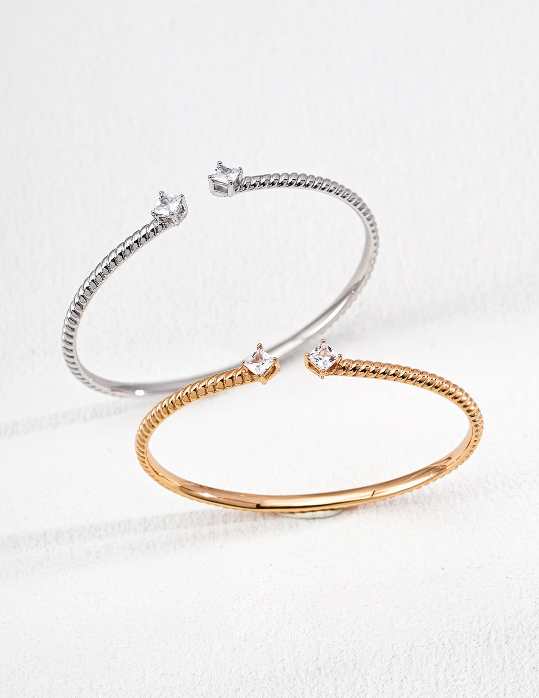 Elegant twisted open cuff bracelet in sterling silver and gold vermeil with zircon accents, styled on a minimal white background.