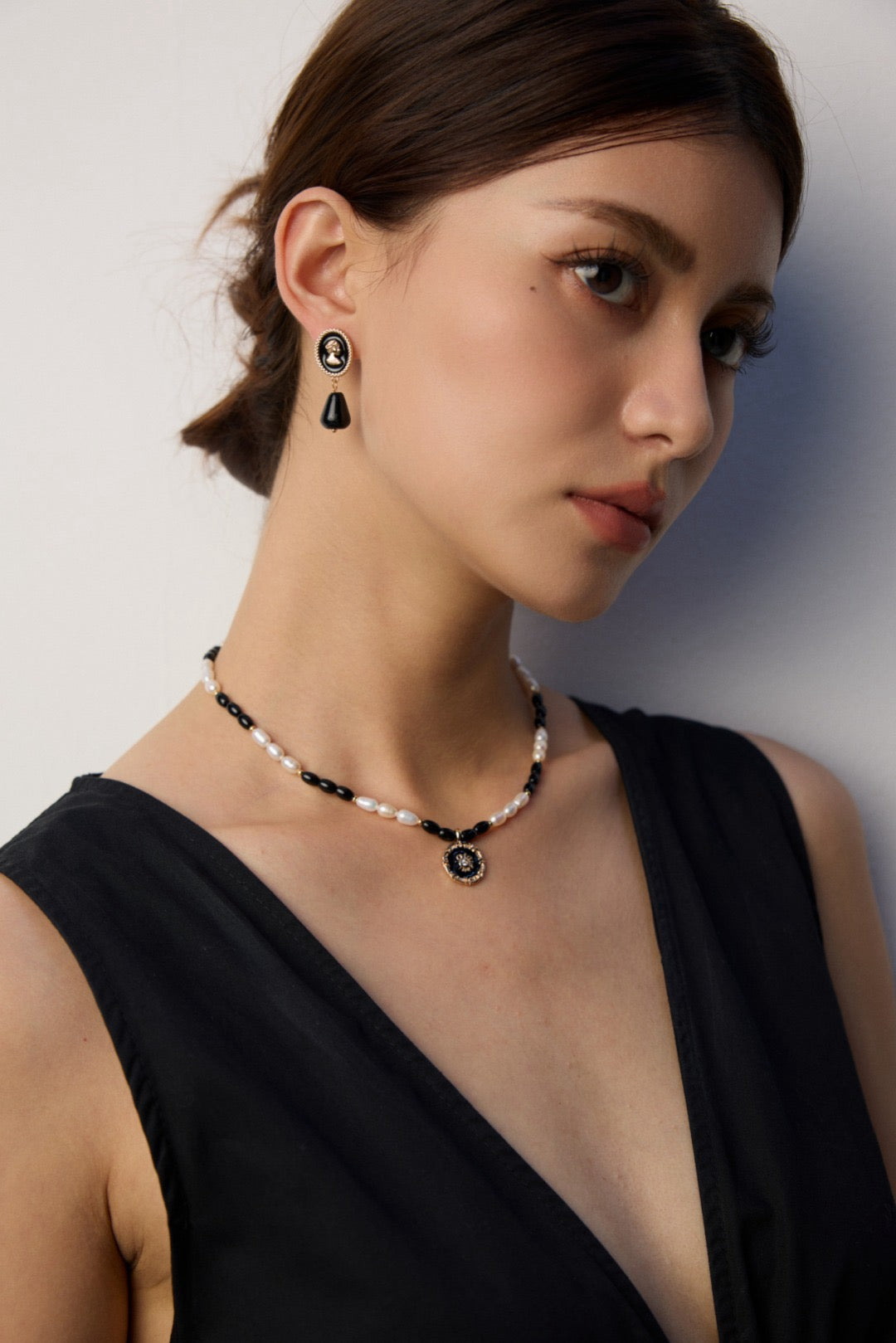 Woman wearing a black and white necklace with matching earrings against a neutral background