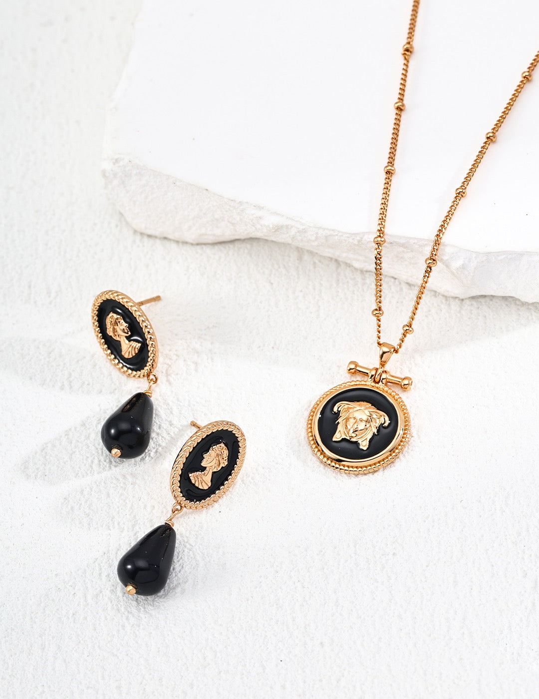 Vintage gold cameo necklace and earrings with black stones on a white fabric background