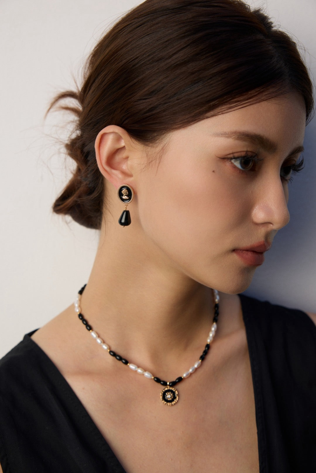 Woman wearing black and white beaded necklace and earrings against a plain background