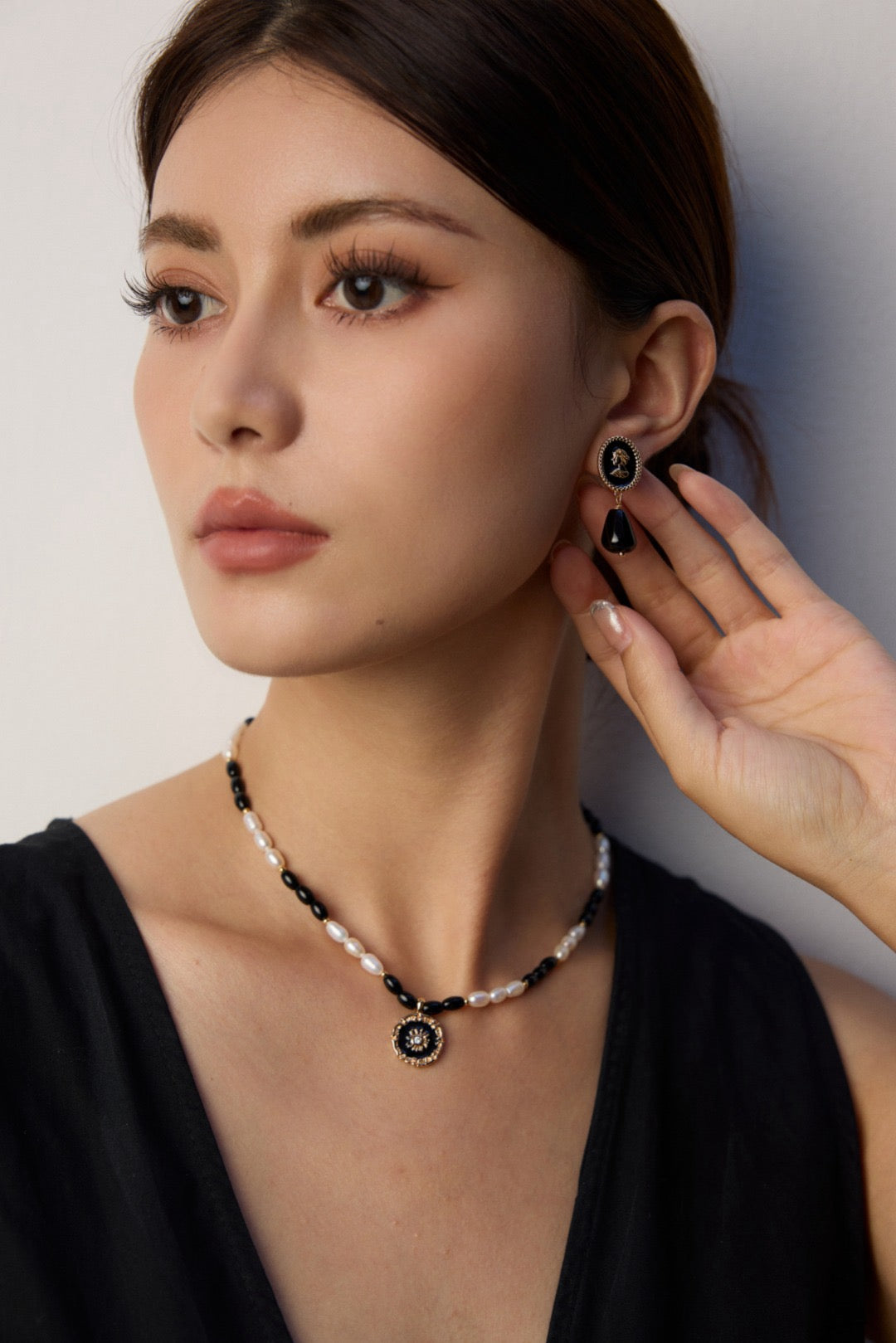 Woman wearing a black cameo earring and necklace against a neutral background