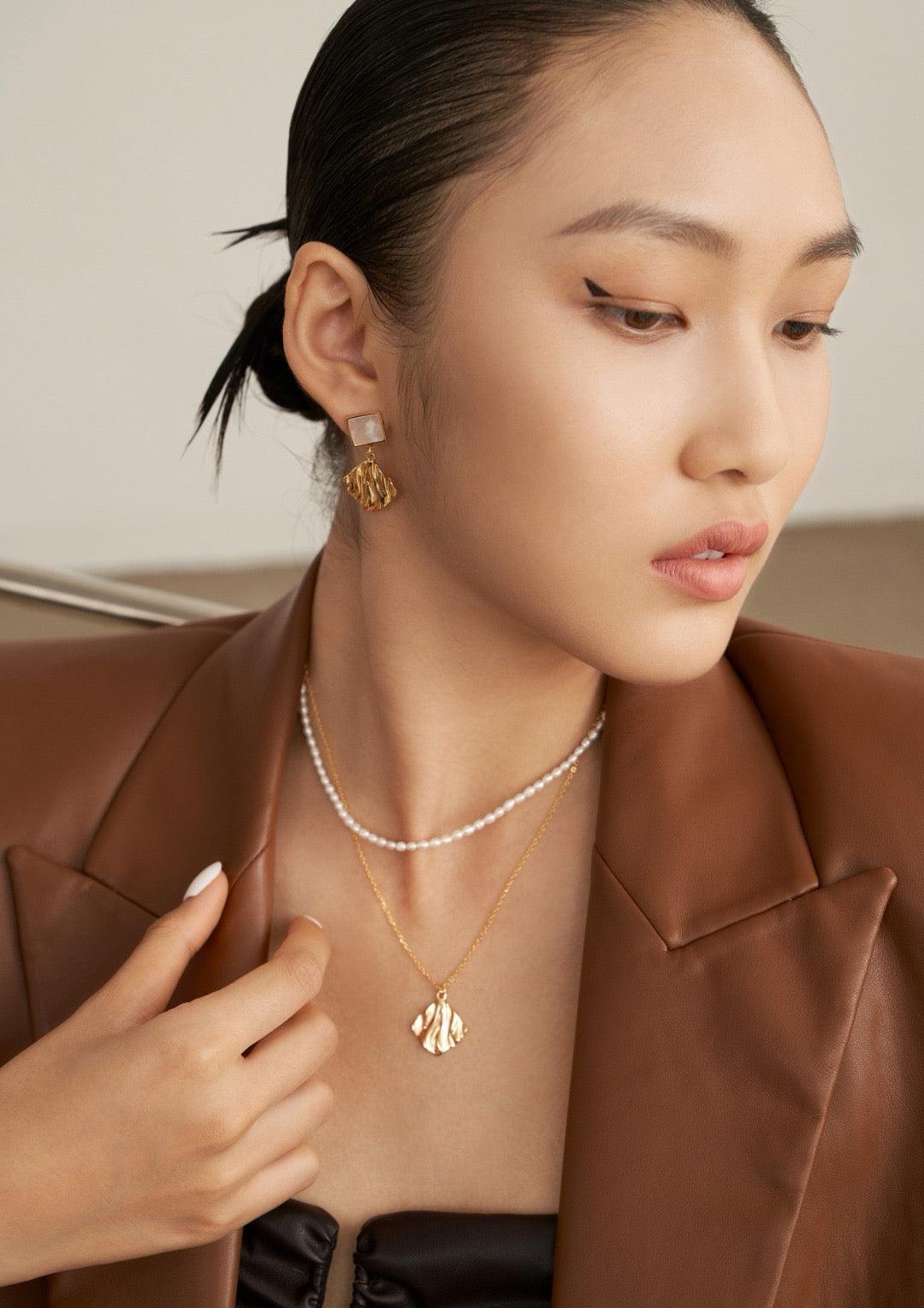 The model is wearing the pearl-layered pendant necklace in a black dress and a brown leather jacket, an effortless style.