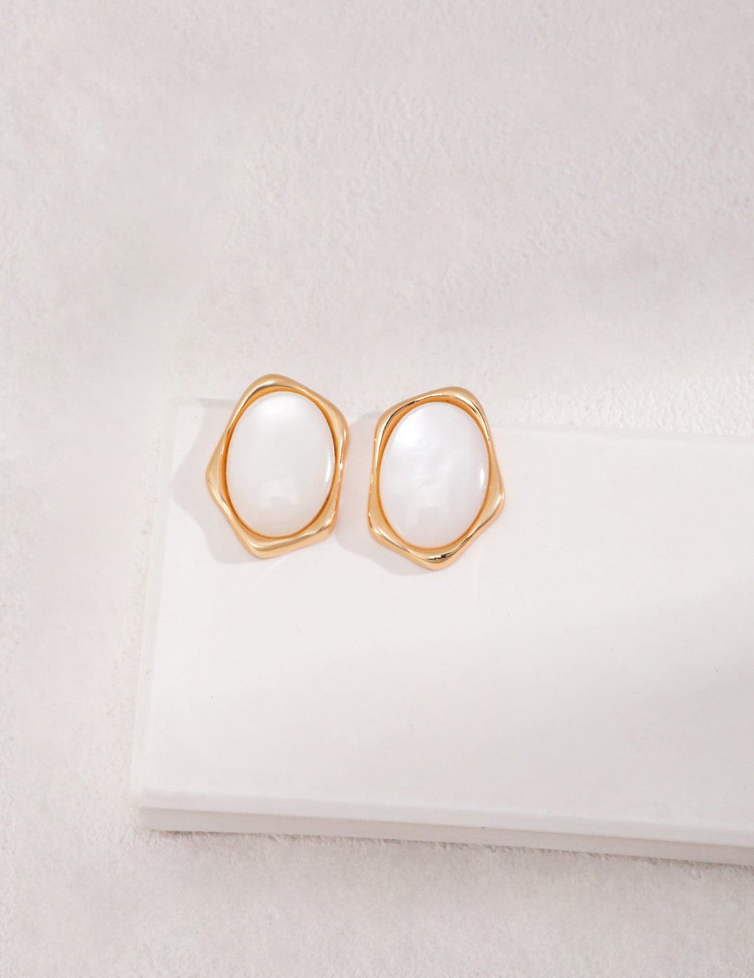 White Mother Of Pearl Stud Earrings In 18K Gold are displayed on the white block.
