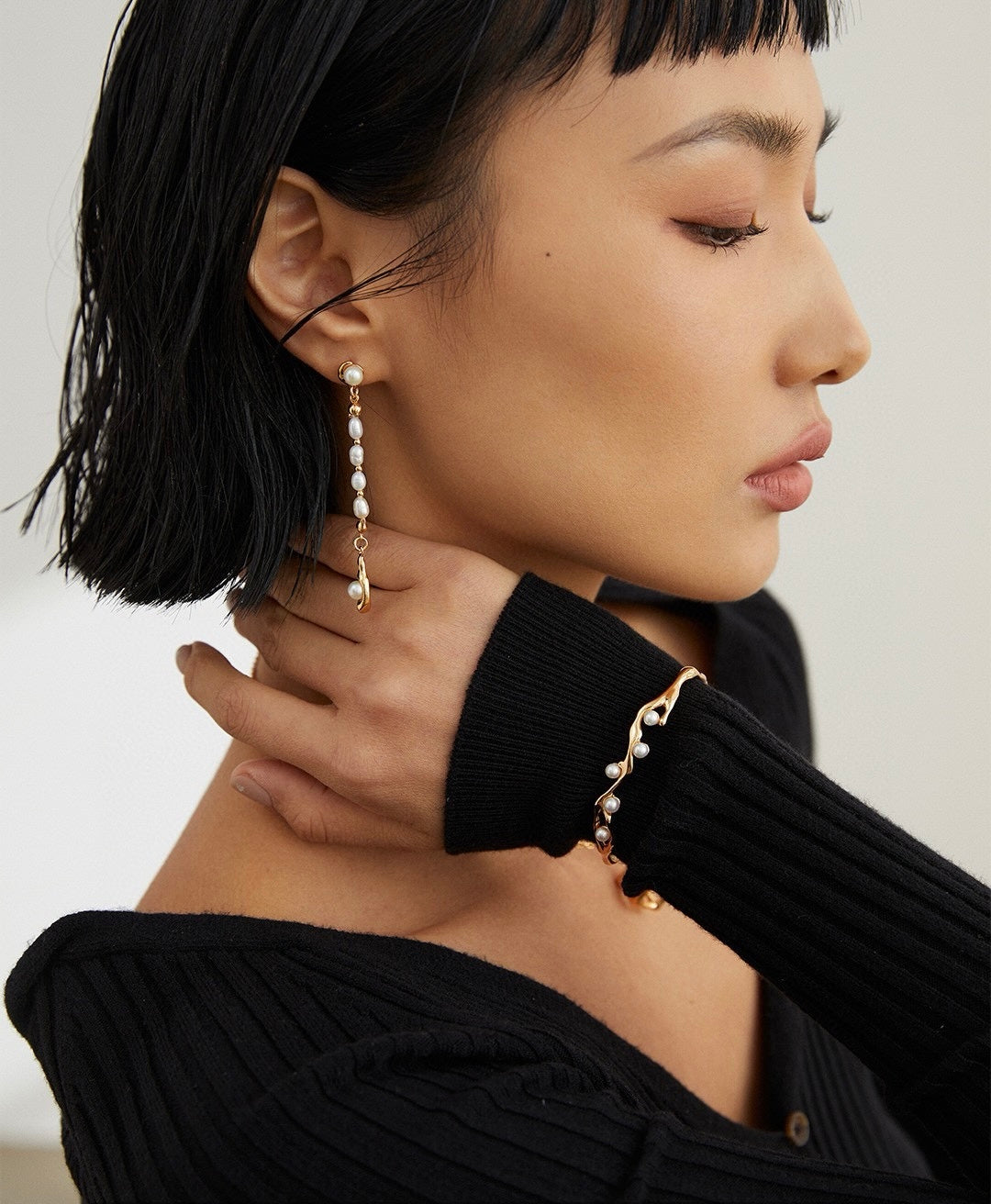 Close-up of a person wearing pearl earrings with a neutral background