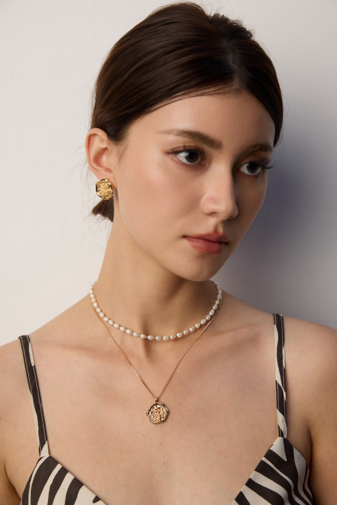 Woman wearing a pearl necklace and earrings against a neutral background