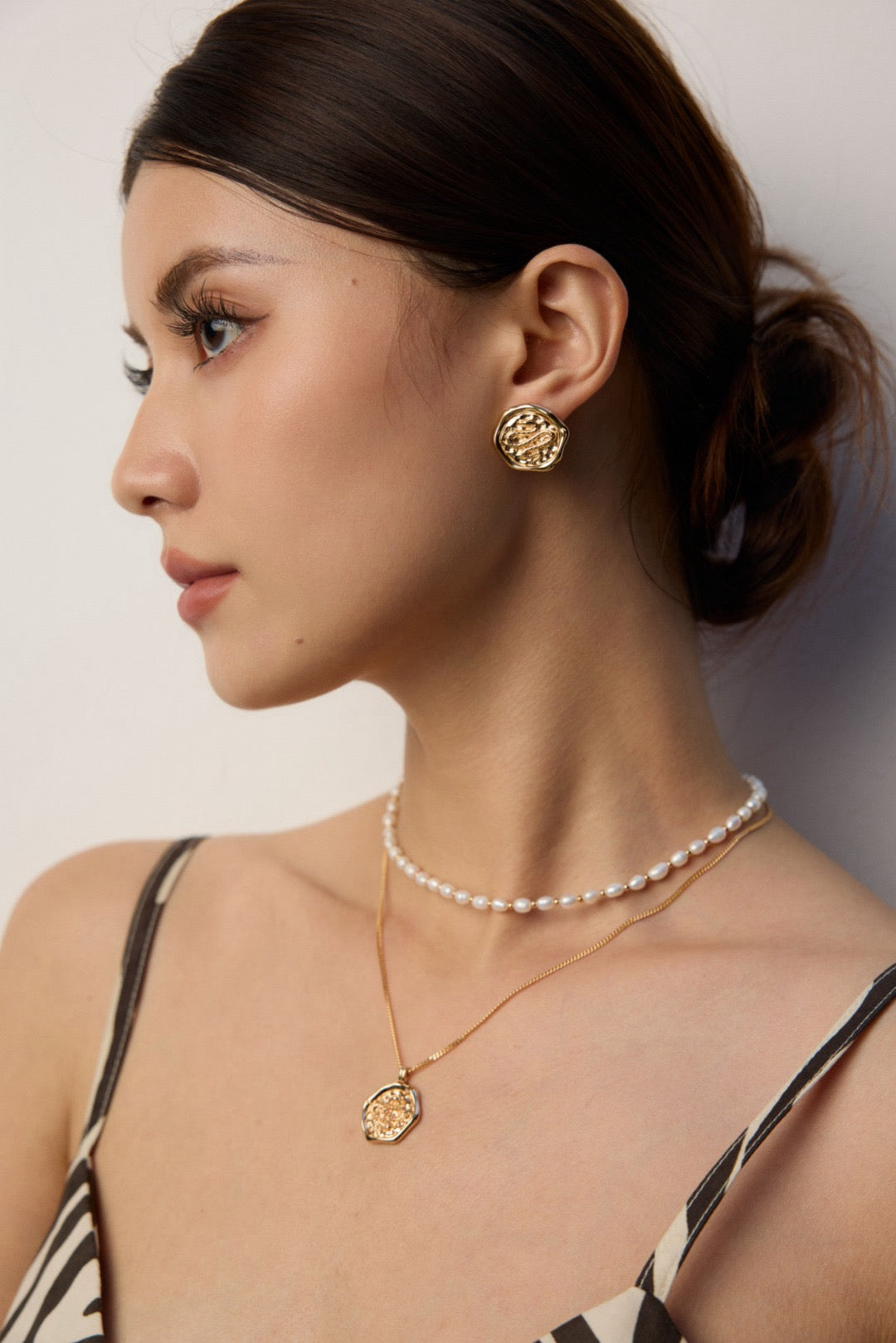 Woman wearing gold earrings and necklace against a neutral background