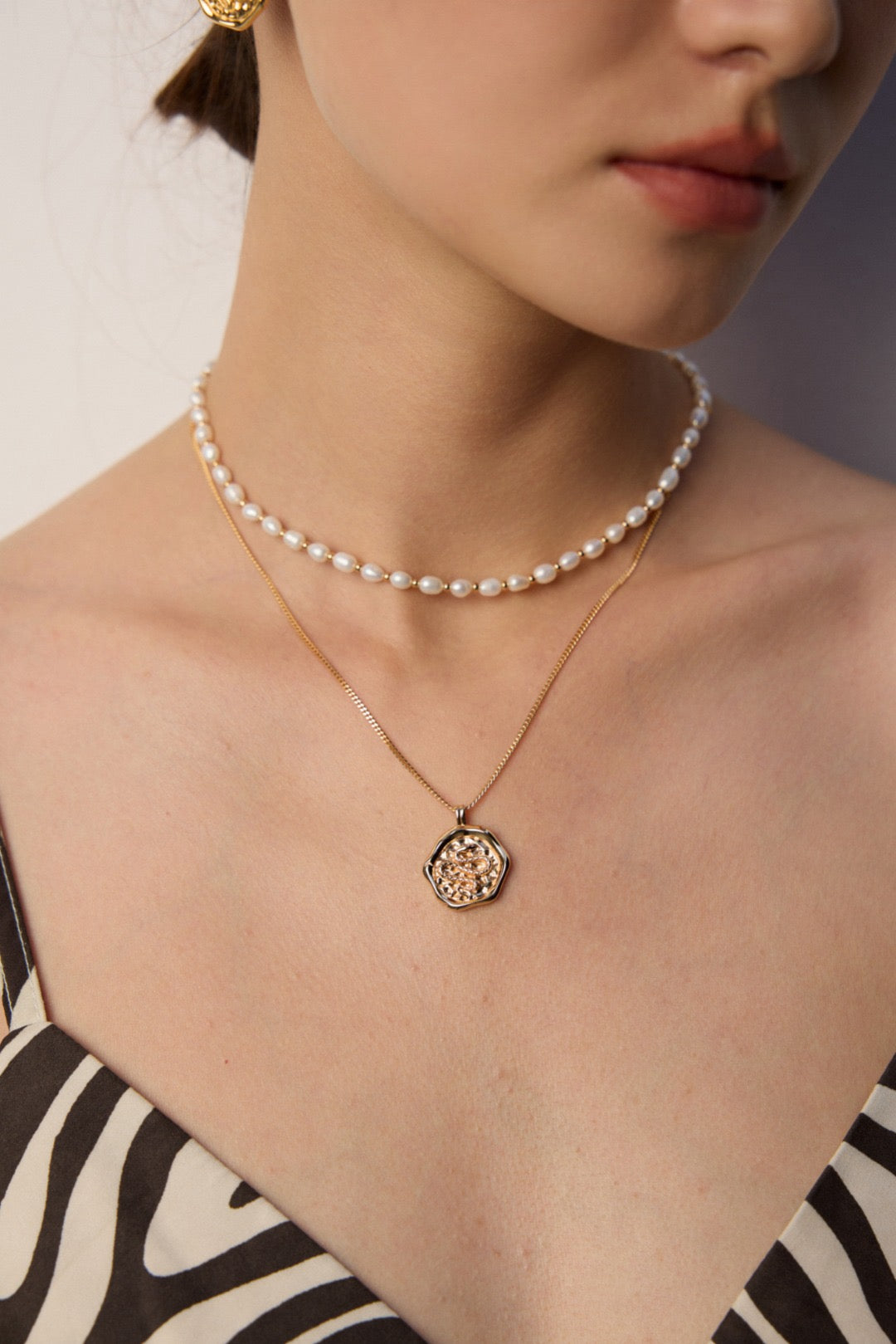 Close-up of a person wearing a pearl necklace and a gold pendant necklace.