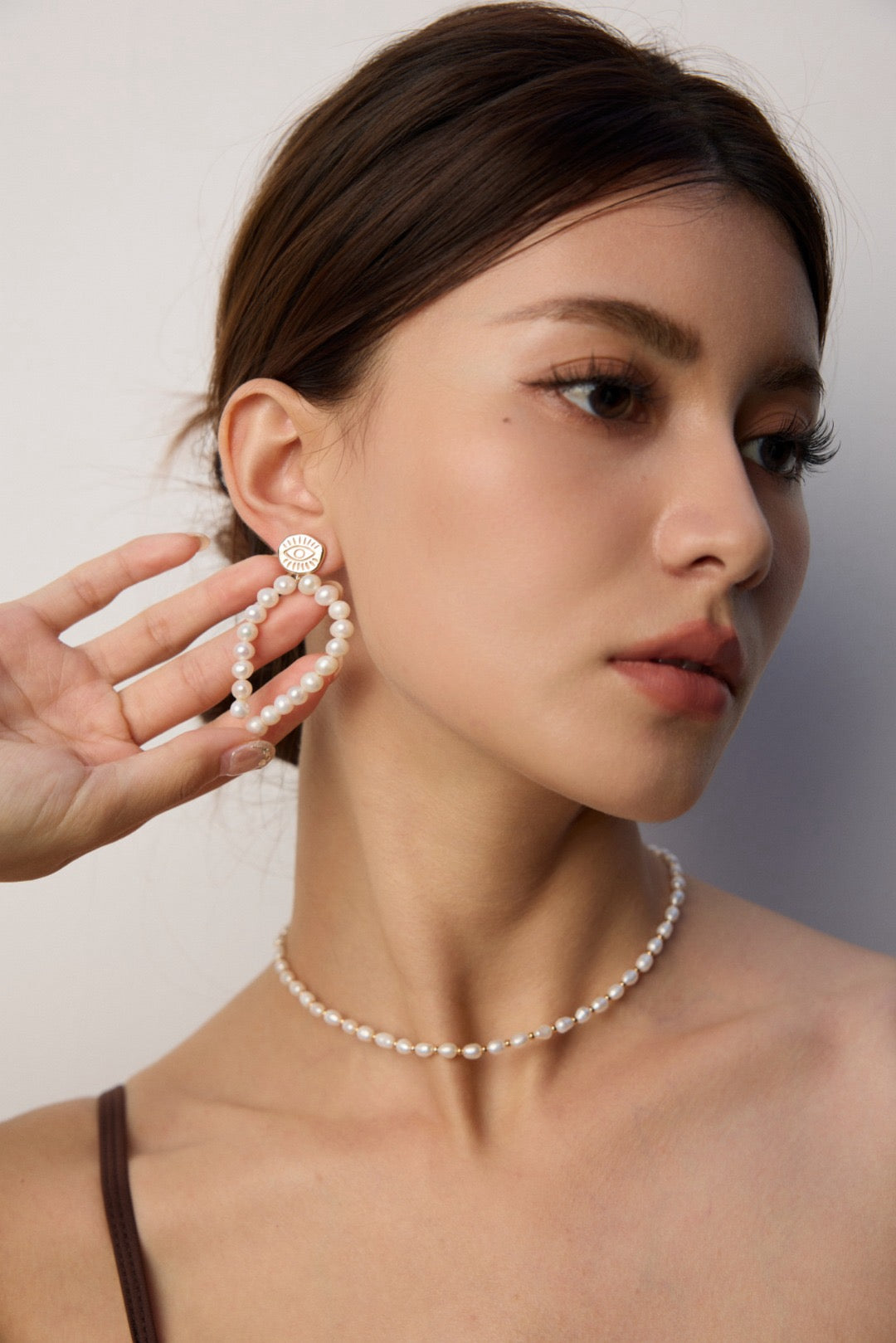 Woman wearing a pearl earring and necklace against a plain background