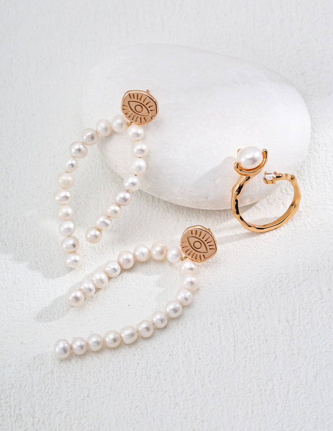 Pearl necklace and earrings with gold evil eye pendants on a white surface