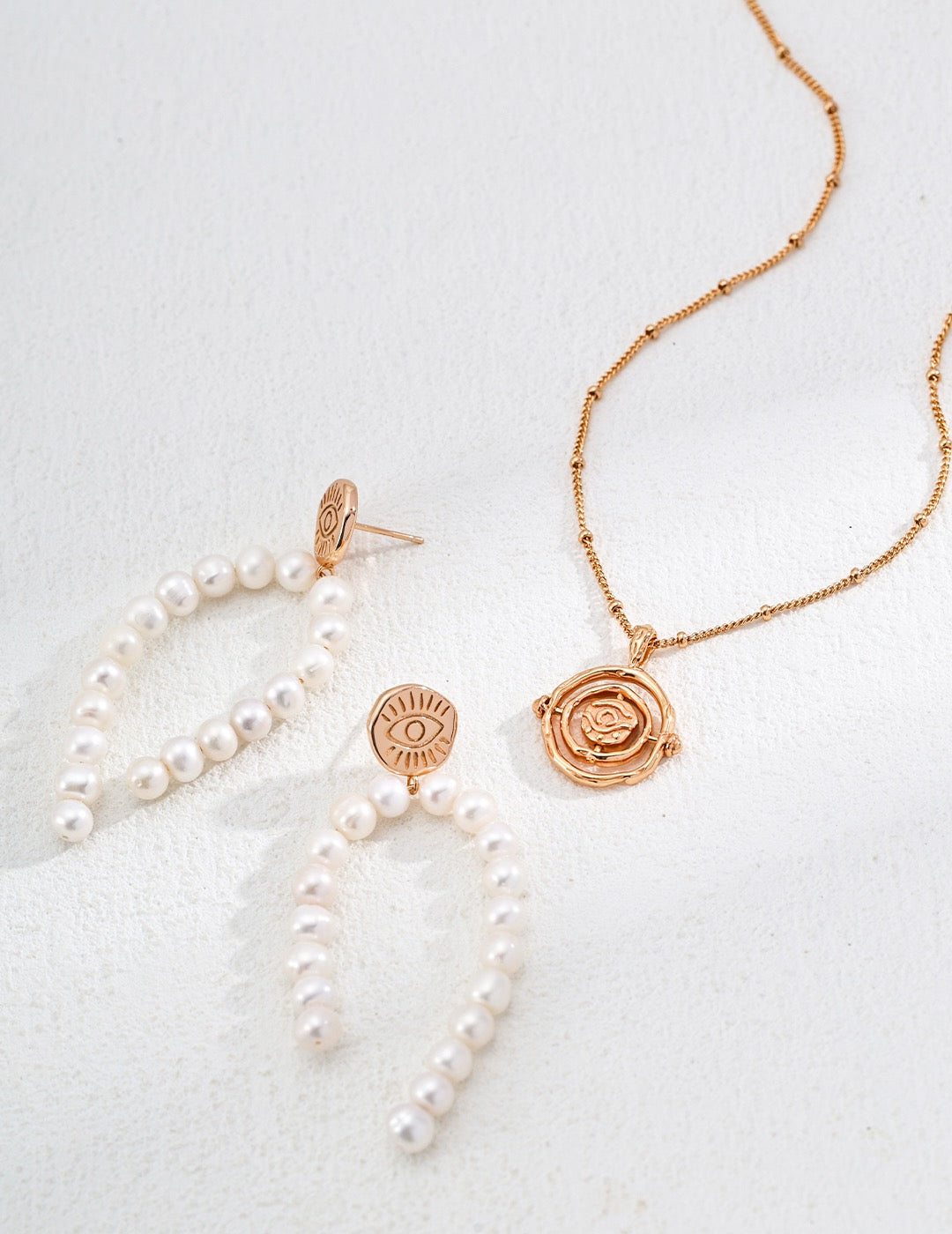 Jewelry set with pearl necklace, earrings, and rose gold pendant on a light background