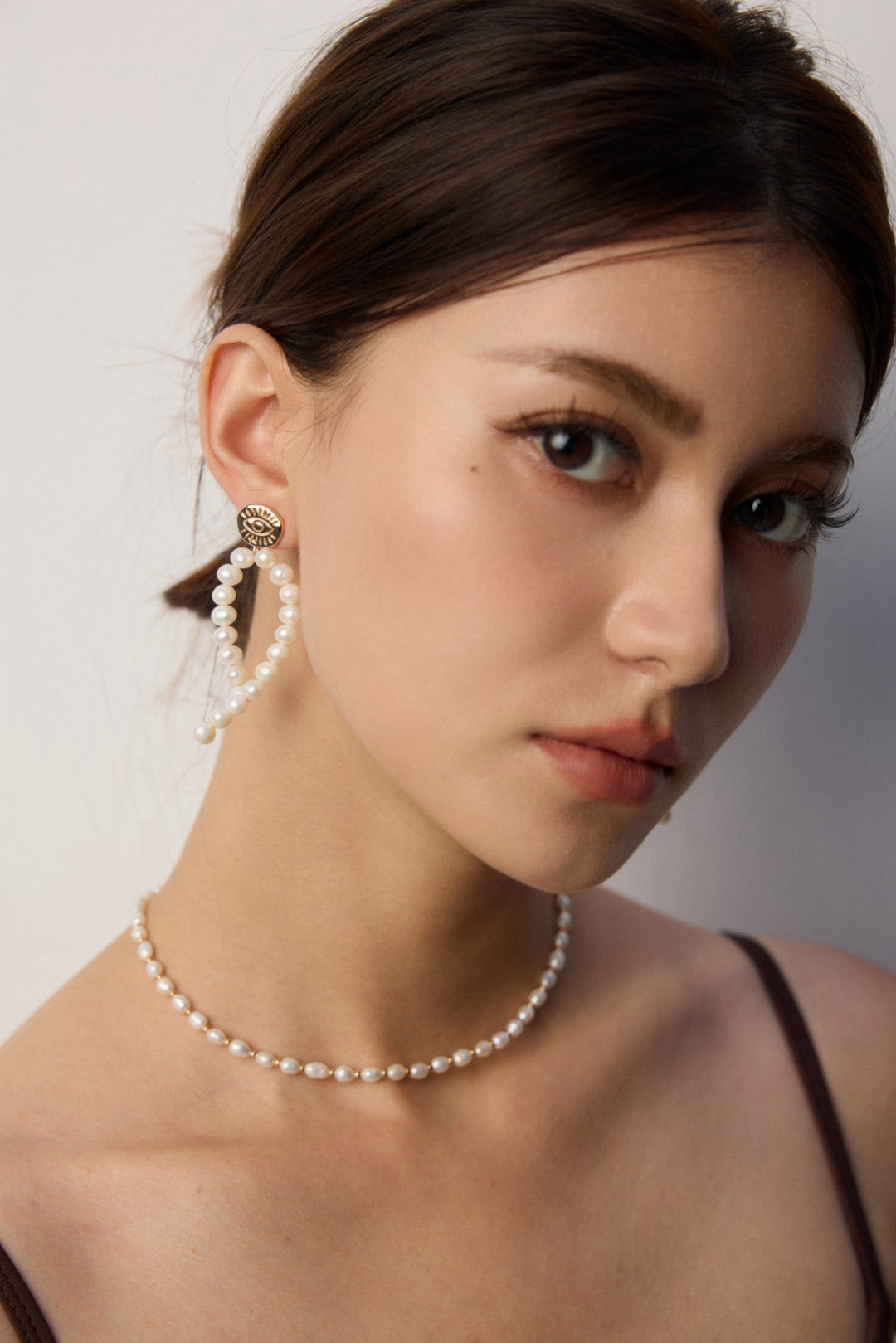Woman wearing a pearl necklace and earrings against a neutral background