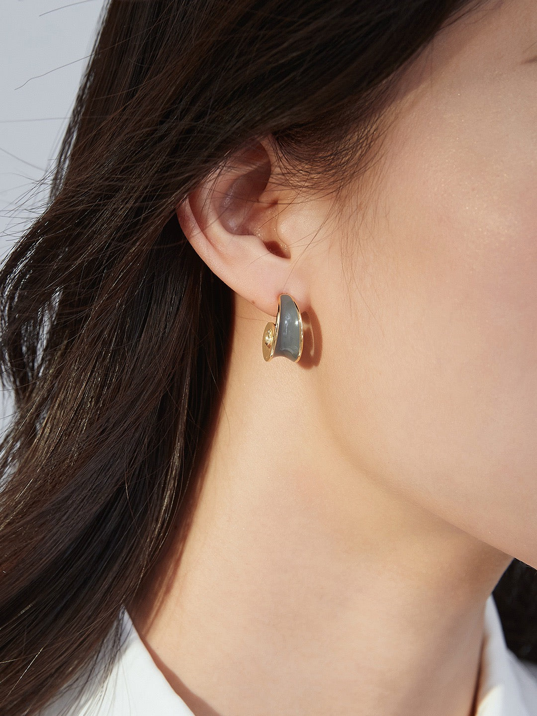 Close-up of an ear wearing a gold and grey earring with a blurred background