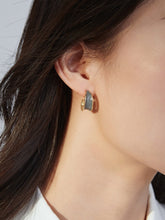 Close-up of an ear wearing a gold and grey earring with a blurred background