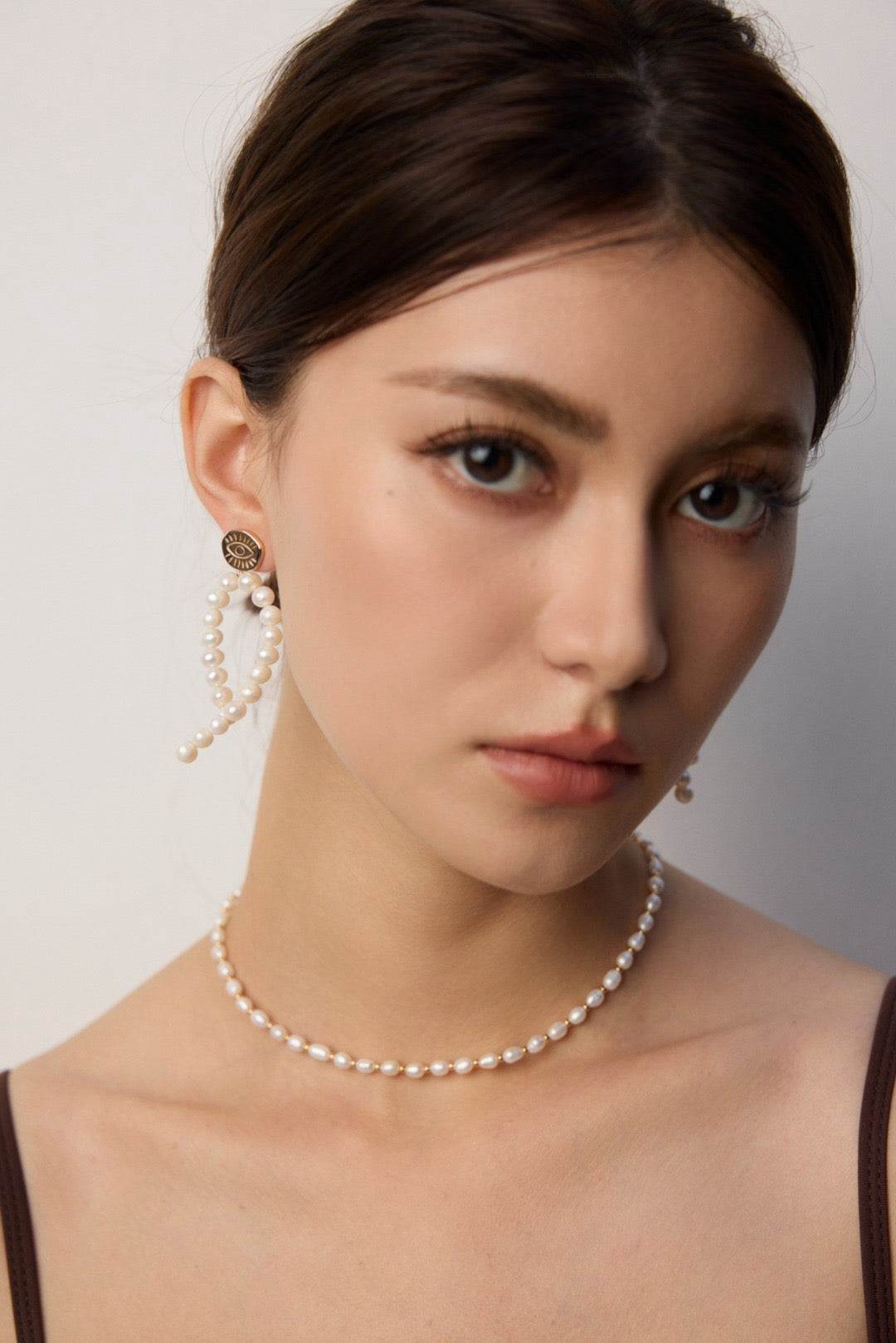 Woman wearing pearl necklace and earrings against a neutral background
